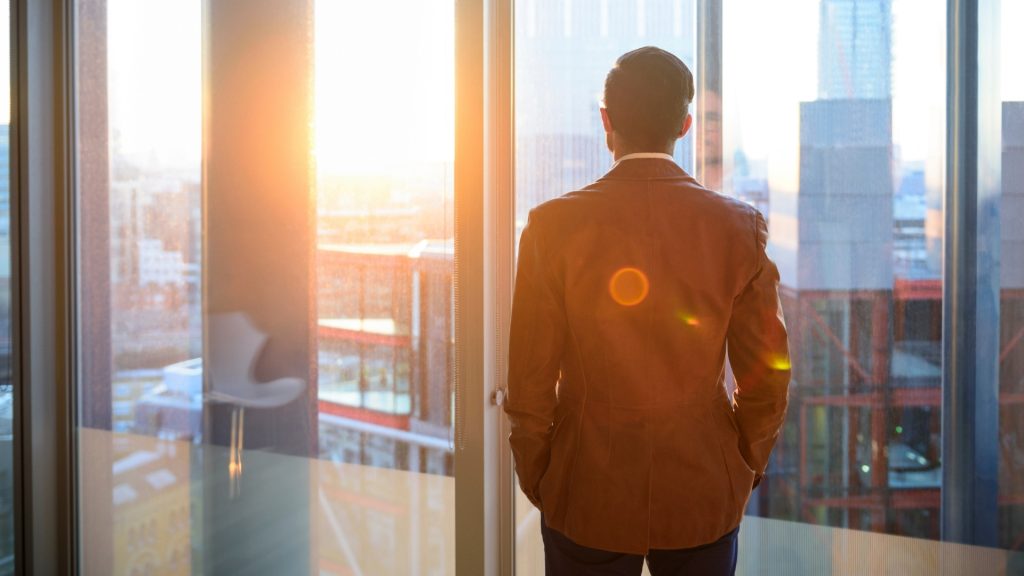 a man in business attire looking out of an office window